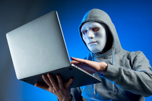 Masked person using laptop, symbolizing cybersecurity threats and computer security risks